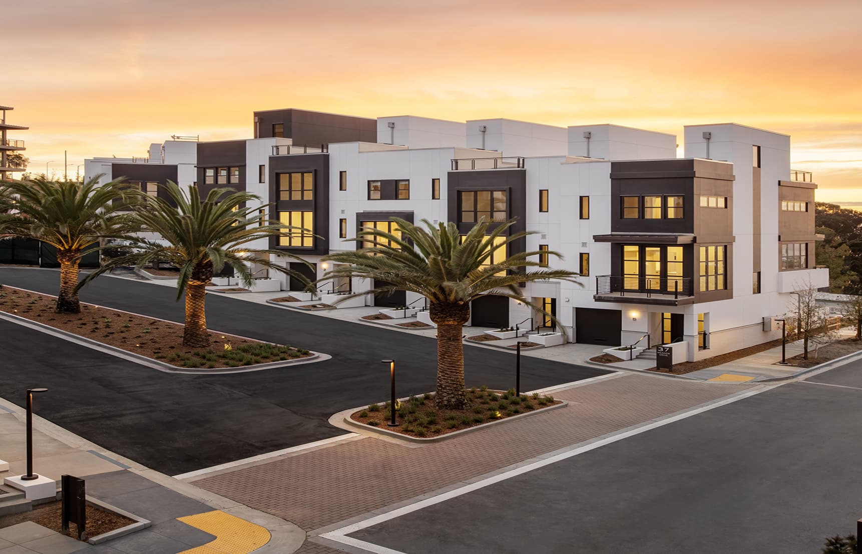 Modern townhomes at The Row on Treasure Island featuring contemporary architecture, palm-lined streets, private garages, and sunset sky over San Francisco Bay.