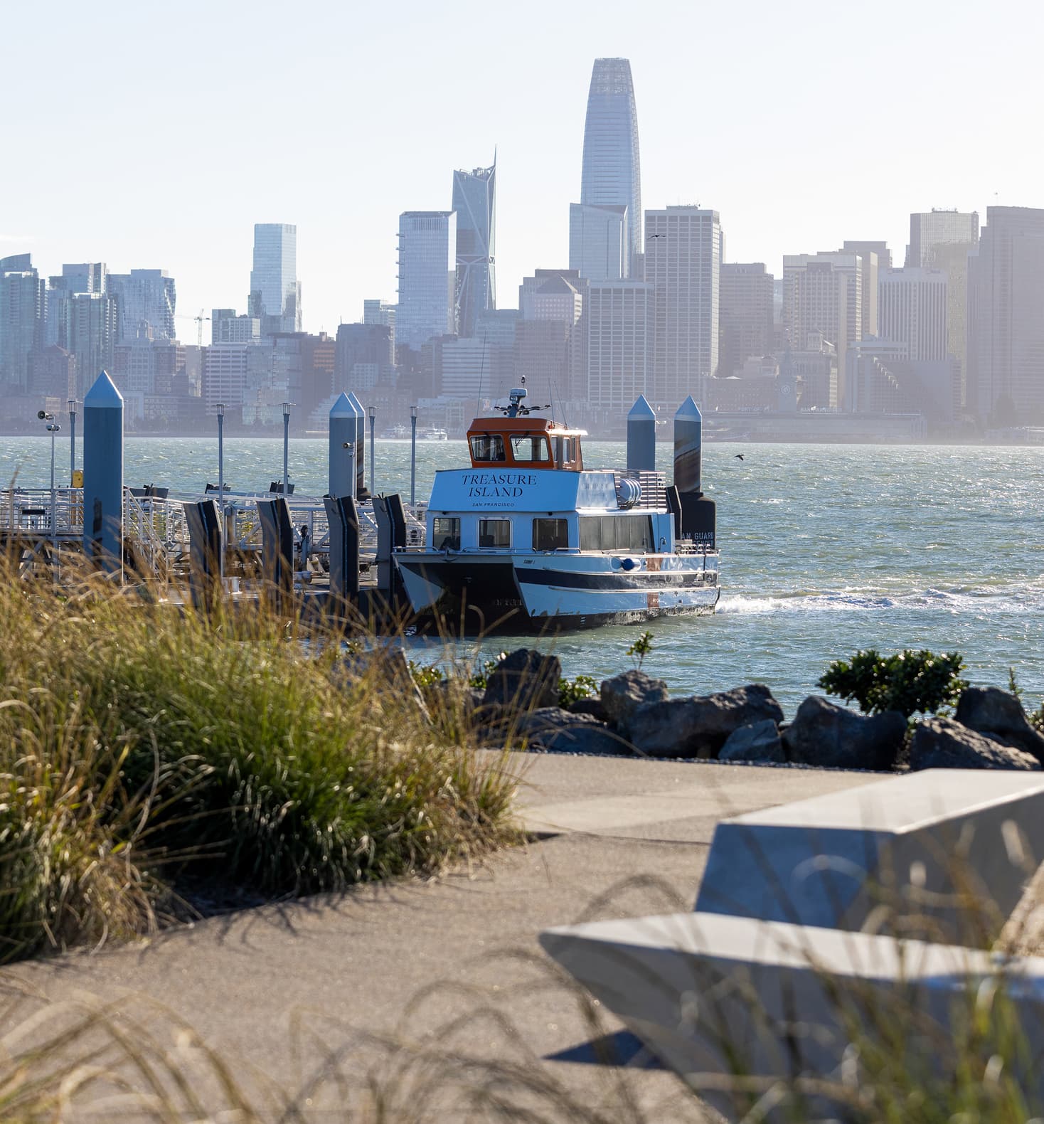 Treasure Island ferry departing a waterfront dock with the San Francisco skyline in the background, showcasing bay transportation and city views on a sunny day.