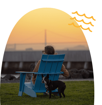 Woman sitting in a lounge chair in a waterfront park on Treasure Island, facing the San Francisco skyline and Bay Bridge across the bay.