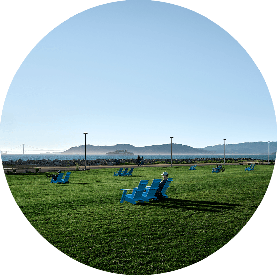 Wide lawn at Cityside Park with bright blue chairs facing the waterfront, with the Bay and distant hills under a clear sky.